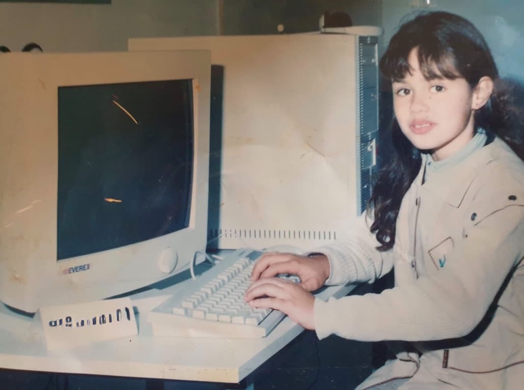Sinda als junges Mädchen, das an einem Desktop-Computer sitzt und die Hände auf der Tastatur hat.